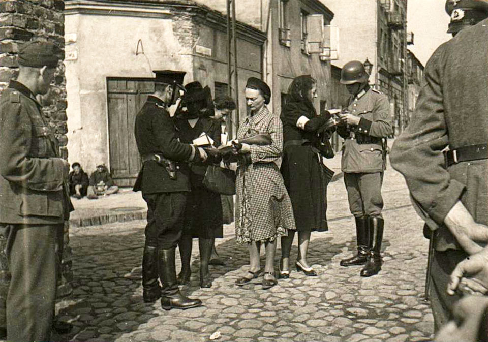 Contrôle des papiers aux environs de la rue Gęsia. Des femmes se dirigent vers le cimetière juif de la rue Okopowa. Des gendarmes allemands et un policier polonais (bleu) effectuent le contrôle. (Photo source inconnue)